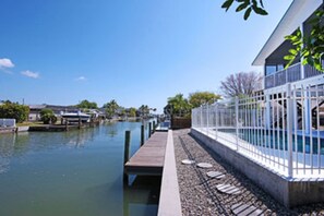 A waterfront property with a dock extending into a calm body of water, a white fence, and a building with a balcony. - Peace and quiet; Private pool - 3BR/3BA (Fort Myers Beach)