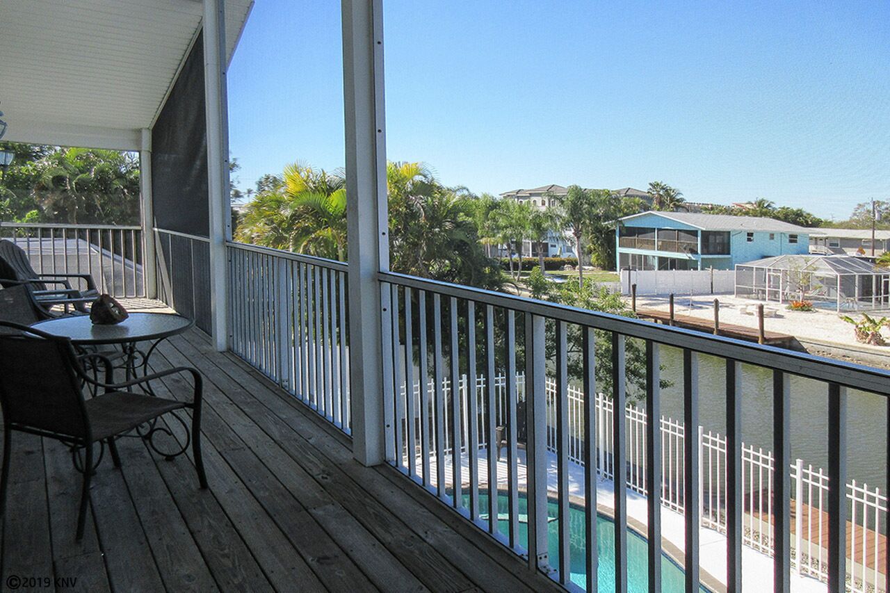 A wooden deck with a pool, a covered seating area, and a view of surrounding buildings.