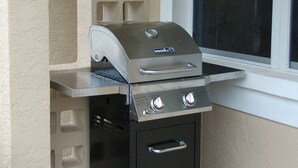 Una griglia barbecue portatile con un armadietto integrato, appoggiata contro un muro con una finestra.
