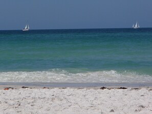 Ein Strand mit weißem Sand und zwei Segelbooten in der Ferne.
