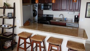 A kitchen with a granite countertop, wooden stools, a microwave, oven, and a sink. - #605 Top Floor Unobstructed Ocean View/Sunsets,  New quiet A.C. (Kihei)