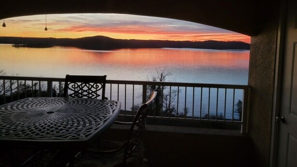 Un balcón con mesa y sillas que da a un lago tranquilo al atardecer.