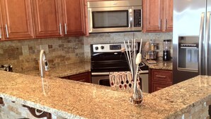 Una cocina con encimeras de granito, una isla integrada, electrodomésticos de acero inoxidable y armarios de madera.