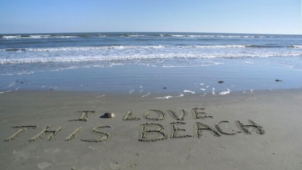 Una playa con las palabras 'I LOVE THIS BEACH' escritas en la arena.