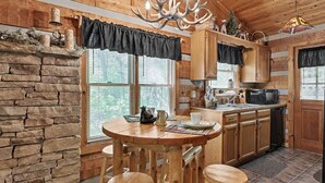 A rustic kitchen with a stone wall, wooden cabinets, a chandelier, and a dining area with stools.