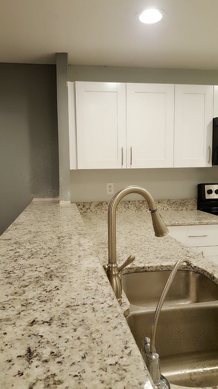 A kitchen with granite countertops, stainless steel sink, and white cabinets.