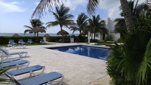 Zona de piscina con sillas de descanso, palmeras y vista al océano.