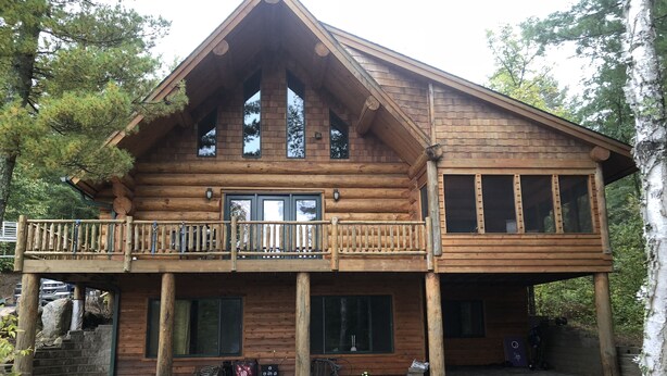 A log cabin with a balcony, large windows, and a stone pathway leading to the entrance. - Log Cabin on beautiful Howard Lake. (Akeley)