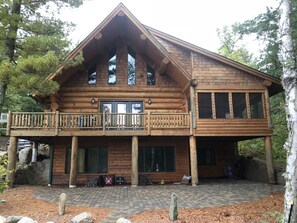 A log cabin with a balcony, large windows, and a stone pathway leading to the entrance.