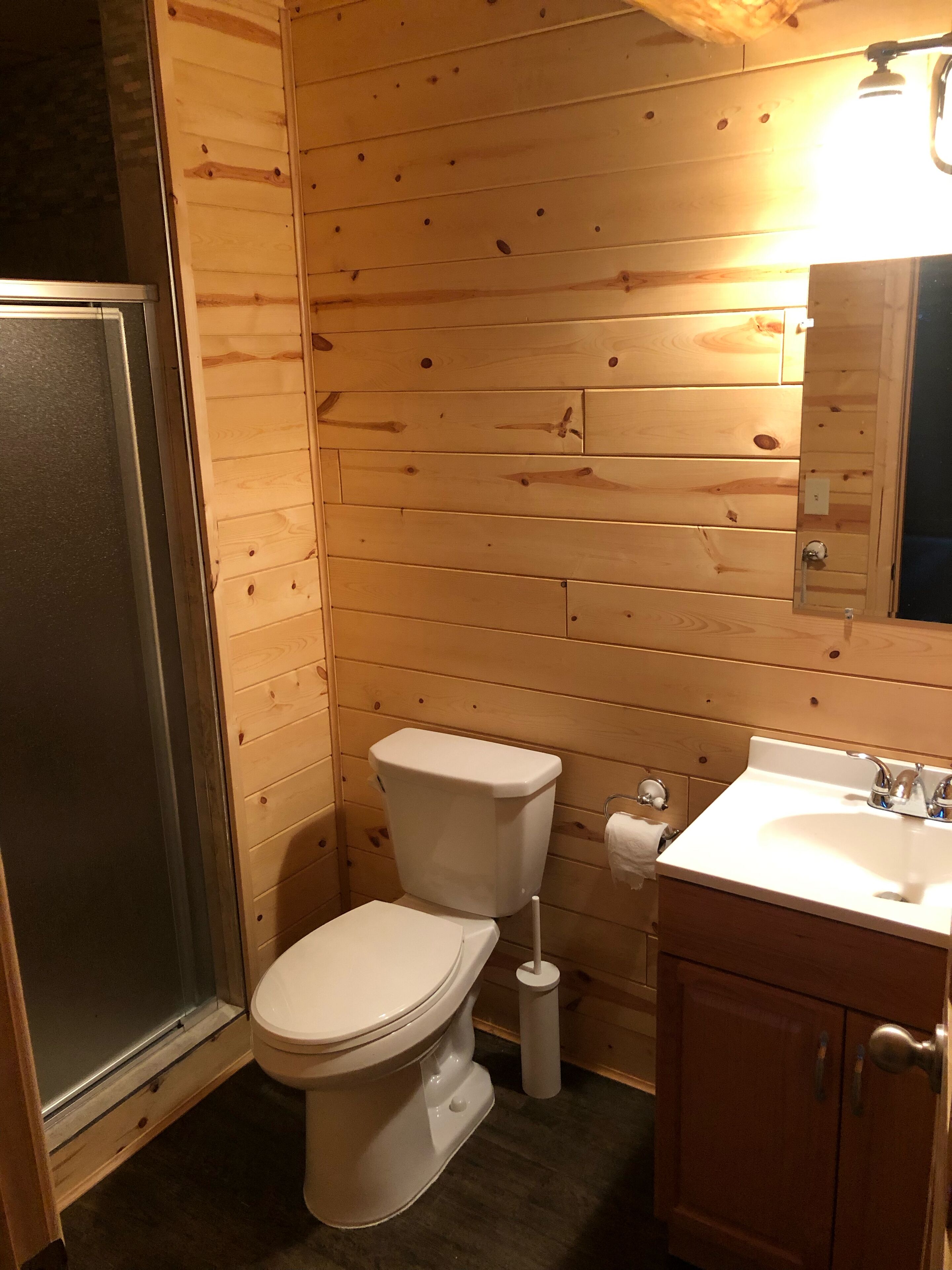 A wooden-paneled bathroom with a toilet, sink, and a mirror.