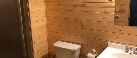 A wooden-paneled bathroom with a toilet, sink, and a mirror.