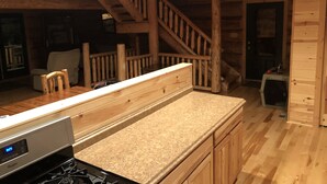 A kitchen with wooden cabinets, a granite countertop, a stove, and a staircase leading to another room. - Log Cabin on beautiful Howard Lake. (Akeley)