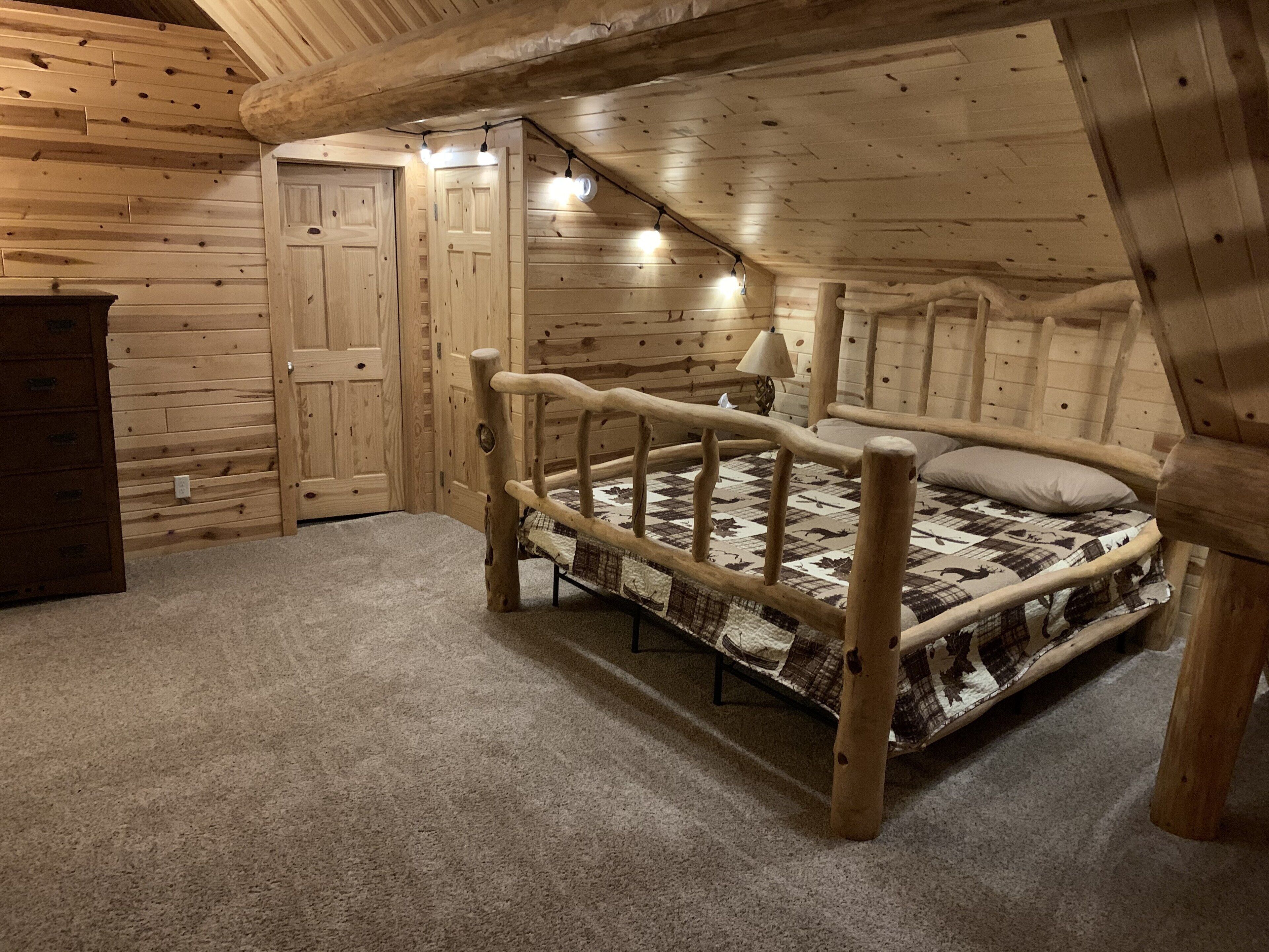 Un dormitorio de cabaña de madera con una cama, un aparador y una puerta.