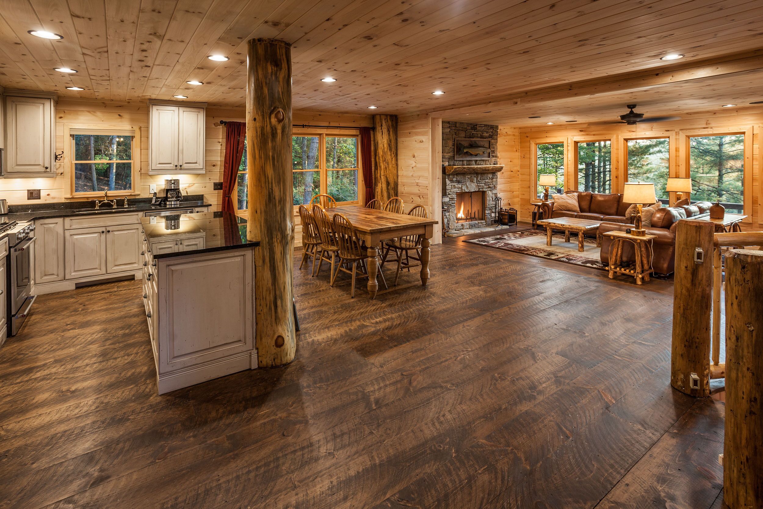 Un interior de cabaña espacioso con comedor de madera, cocina y sala de estar que incluye una chimenea.