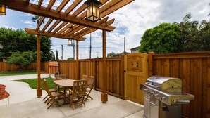 Een terras met een houten pergola, een barbecue en een eettafel met stoelen.