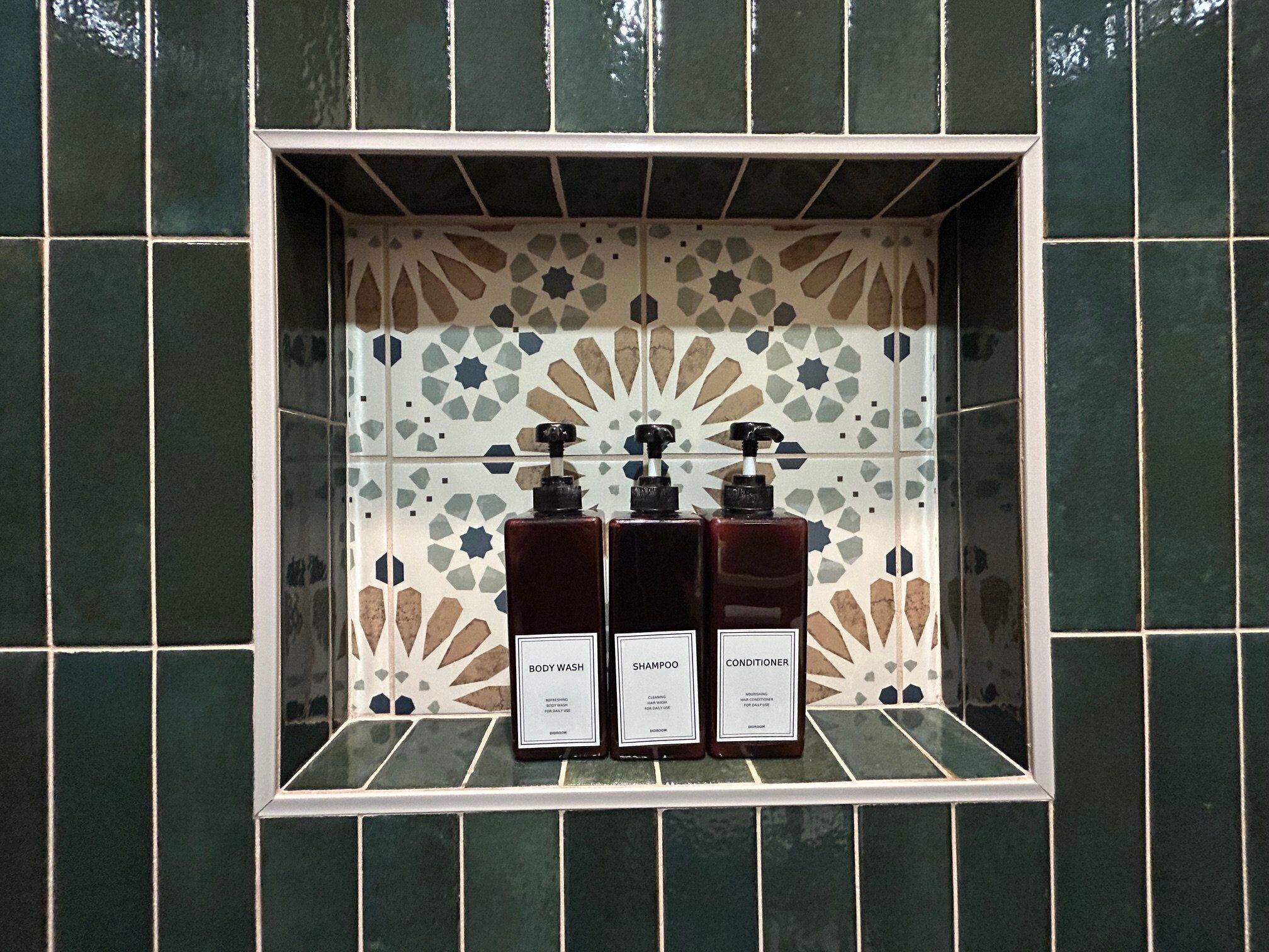 Ein Badezimmer mit einer raumhoch verkleideten Wand und einem Regal mit drei Flaschen – Duschgel, Shampoo und Conditioner.