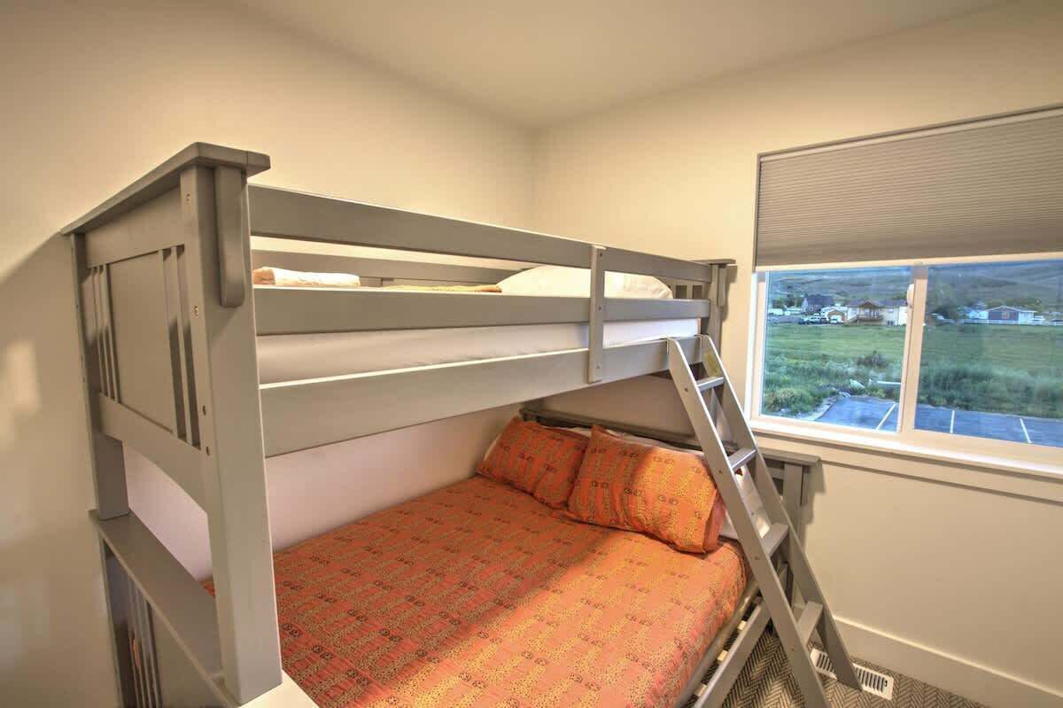 Een stapelbed met een ladder, een bed met een decoratieve spreidek en een raam met uitzicht op een groen landschap.
