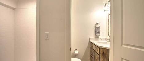 Un baño con ducha, inodoro y tocador con armarios de madera.