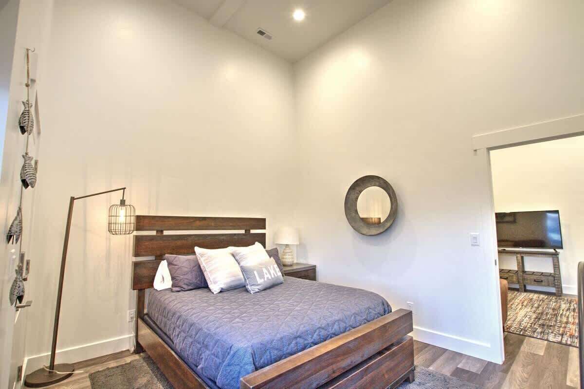 A bedroom with a bed, bedside tables, a floor lamp, a mirror, and a television in the adjacent room.