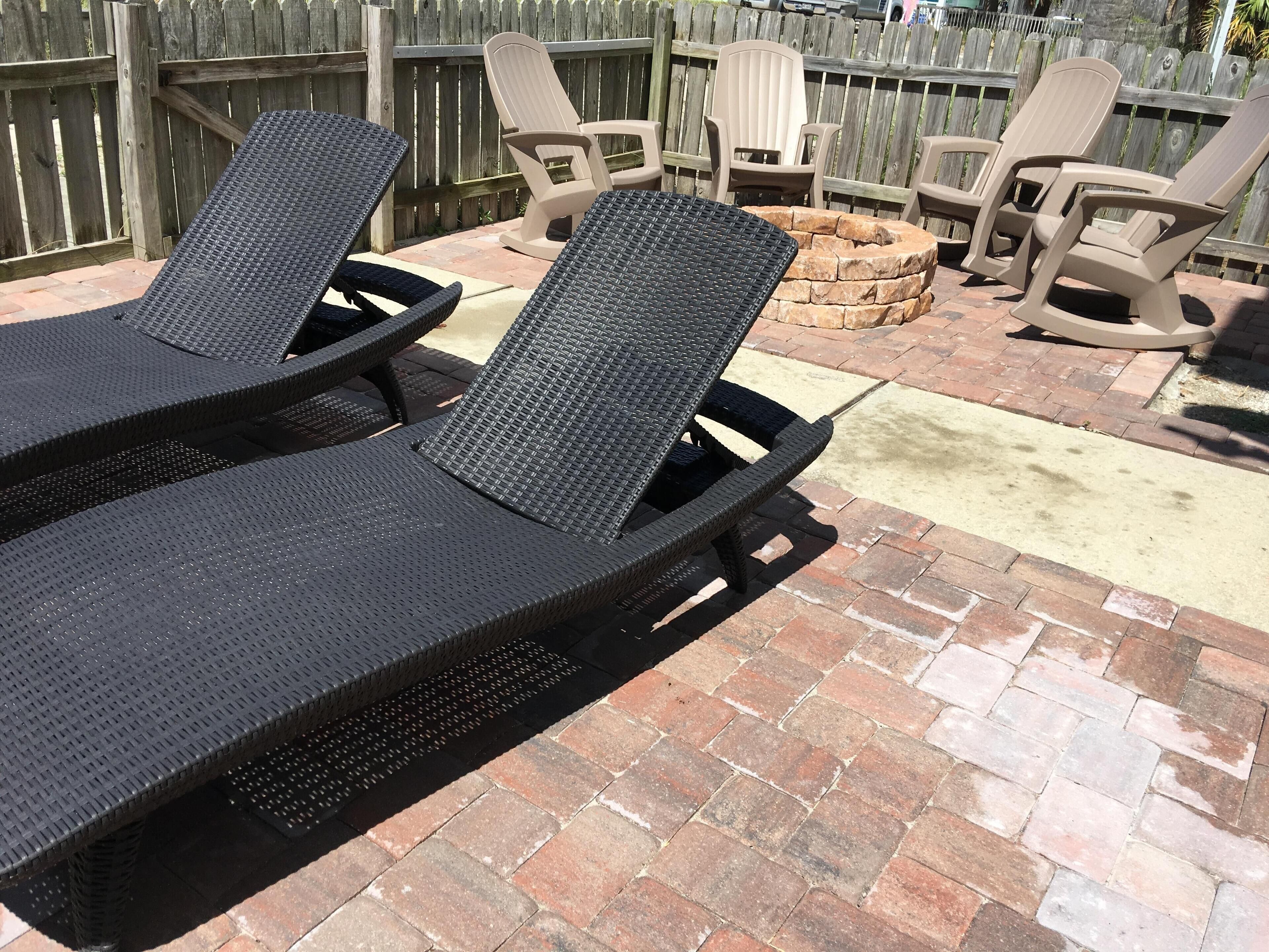 A patio area with two black wicker lounge chairs and a stone fire pit.
