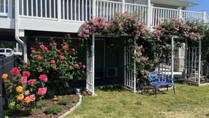 Ett hus med en täckt veranda, vita räcken och rosa blommande växter.