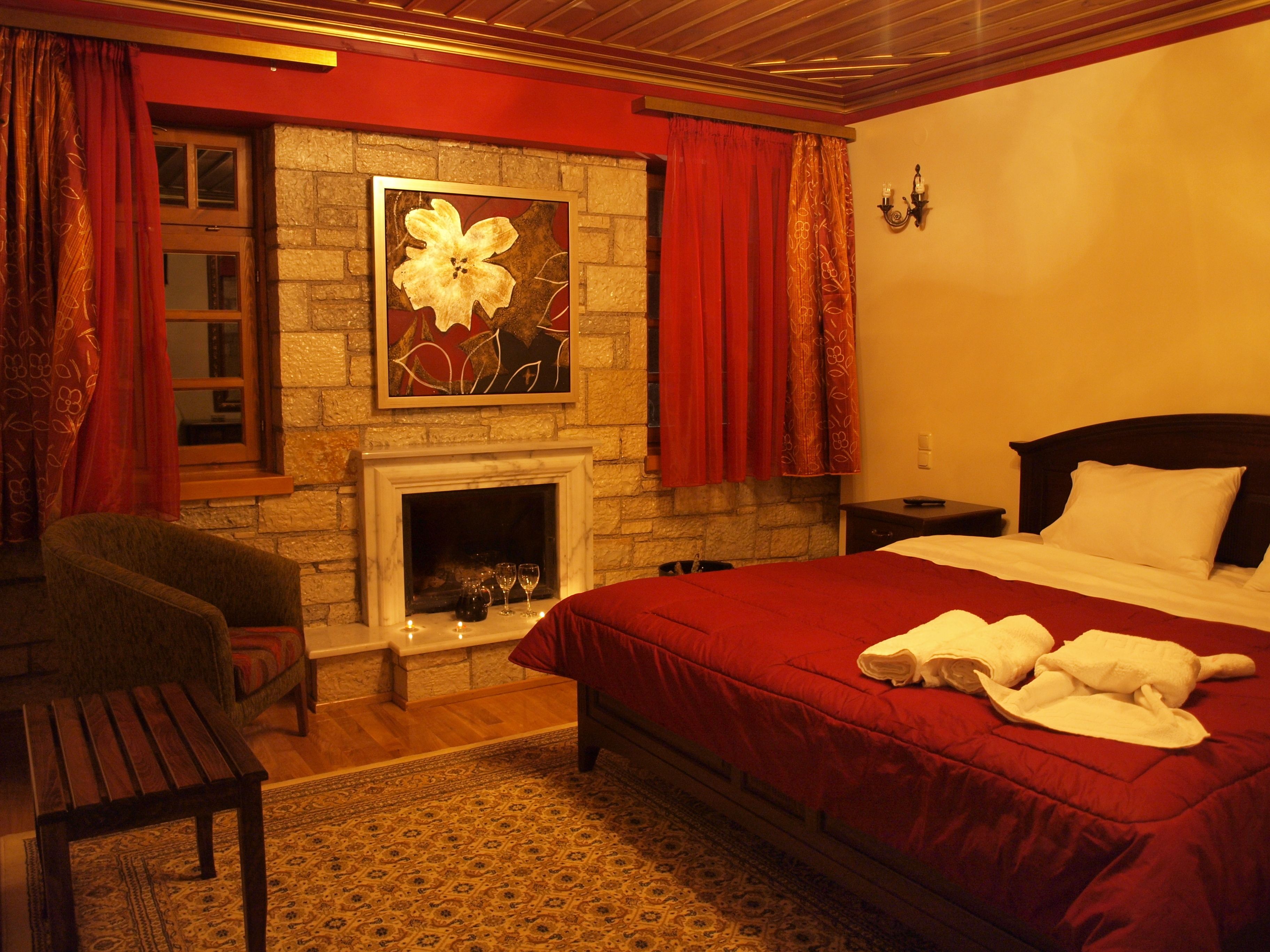 A hotel room with a fireplace, a bed with red bedding, a chair, and a rug.