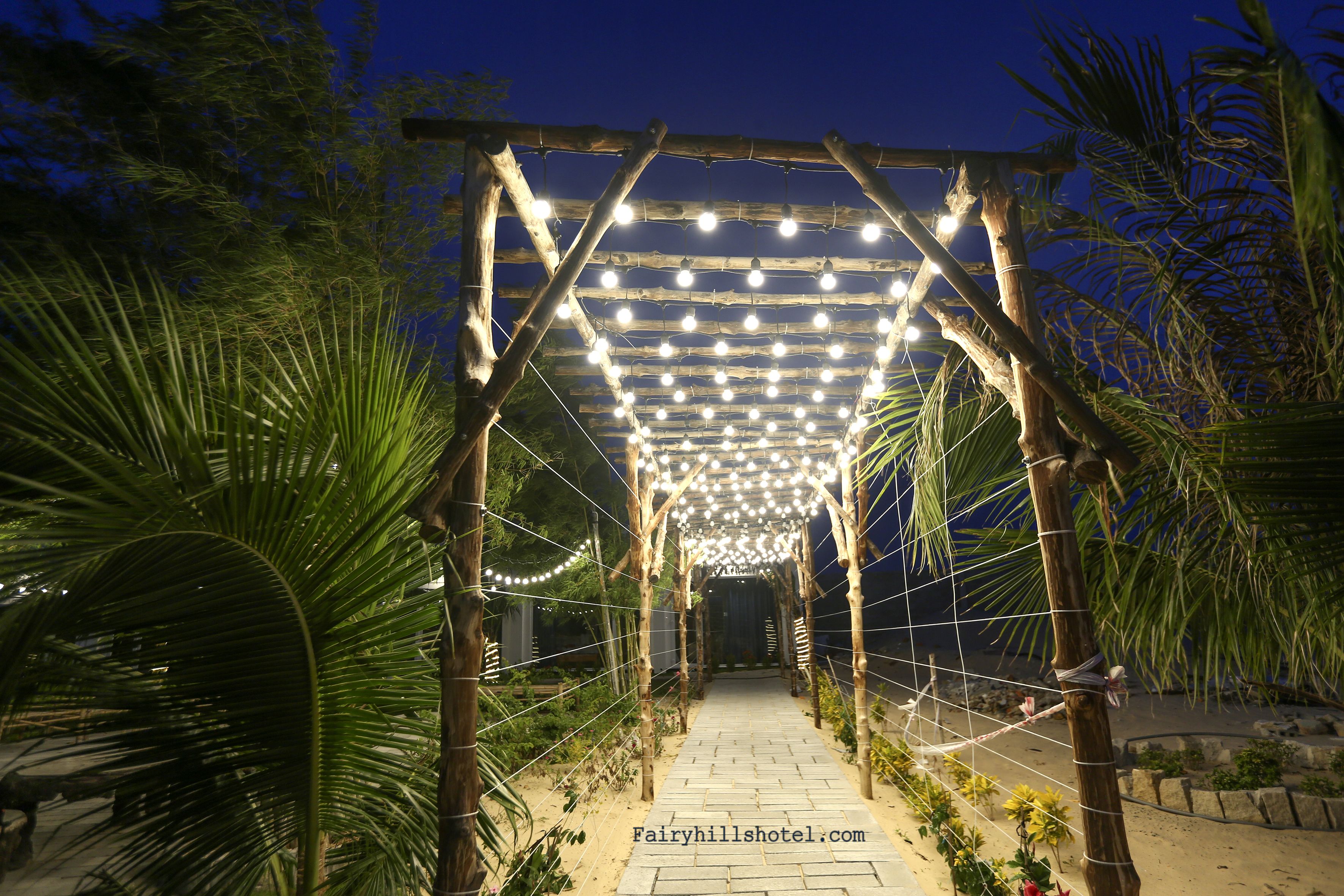 Eine Holz-Pergola mit Lichterketten, umgeben von Palmen und Pflanzen.