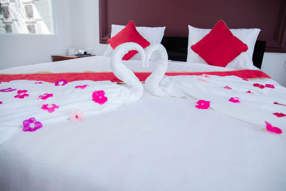 Un letto con cigno di cuscini e fiori rosa sparsi.