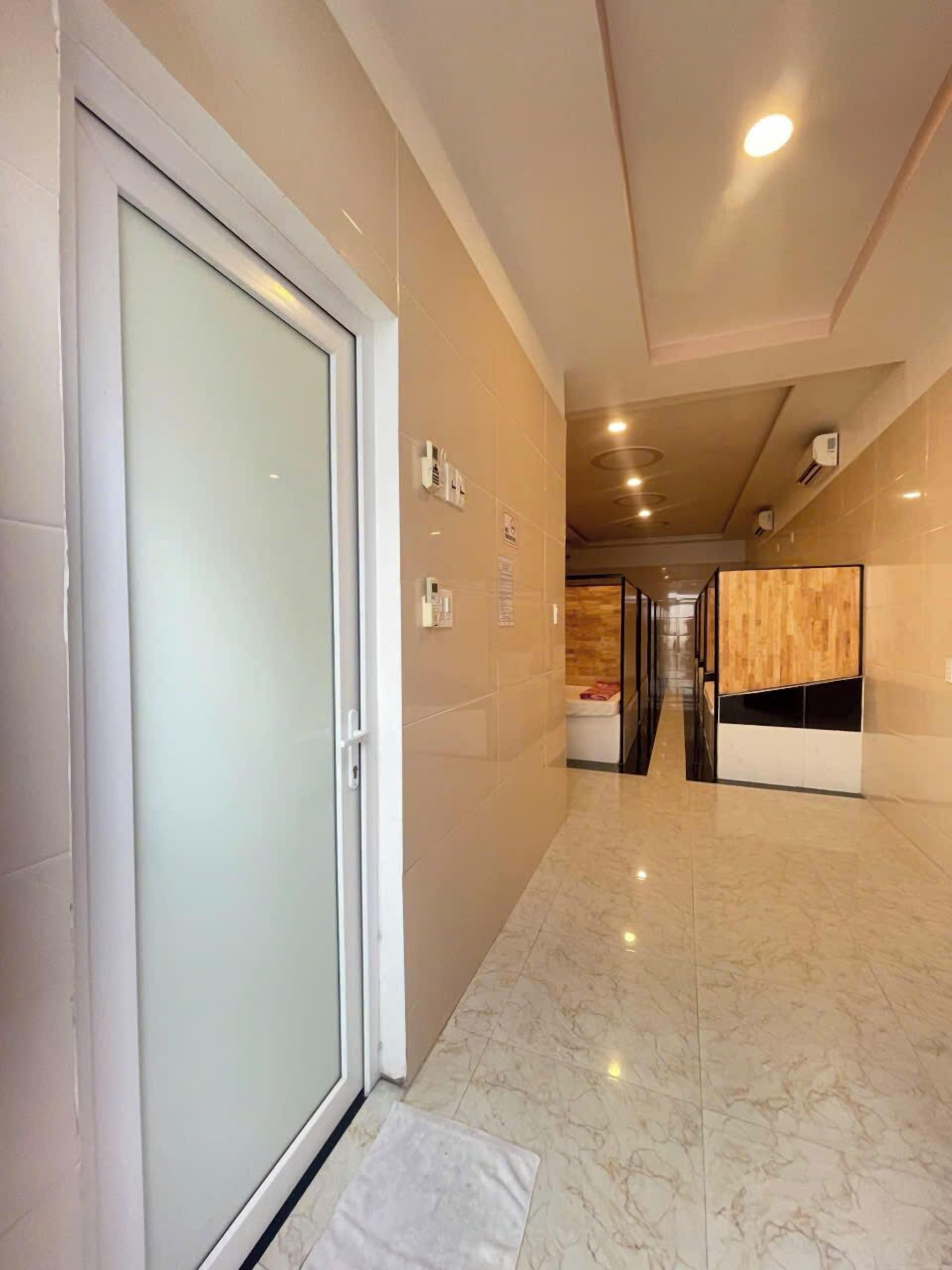 A hotel corridor with a glass door, tiled walls, and a wooden reception desk.