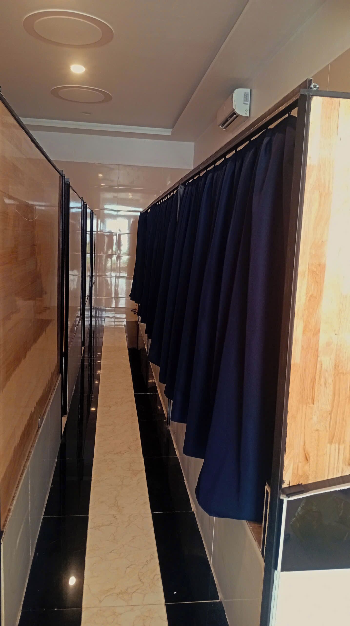 Un corridoio con pavimento a scacchi bianco e nero, una parete in legno da un lato e un'infilata di tende blu scuro dall'altro.
