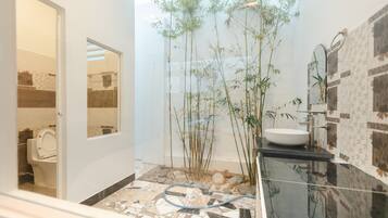 A bathroom with a toilet, a sink, and a mirror. There are bamboo plants and a hosed floor.