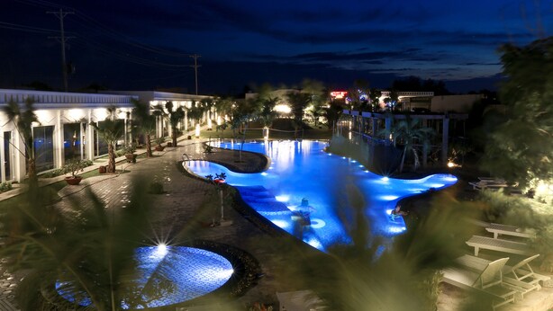A nighttime view of a swimming pool area with a water feature, lounge chairs, and a building with lights. - Suoi TIen Hills Hotel (Mui Ne)