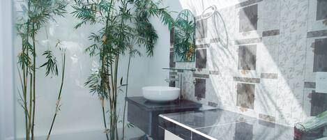 A modern bathroom with a glass shower enclosure, a white sink, and bamboo plants.