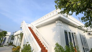 A white building with a staircase leading to the entrance, surrounded by greenery. - Suoi TIen Hills Hotel (Mui Ne)