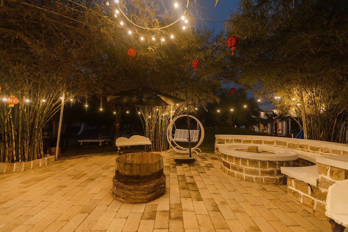 Un'area patio esterna con una panchina in pietra, una botte di legno e una zona salotto circolare.