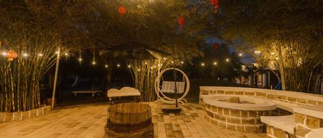 An outdoor patio area with a stone bench, a wooden barrel, and a circular seating area.