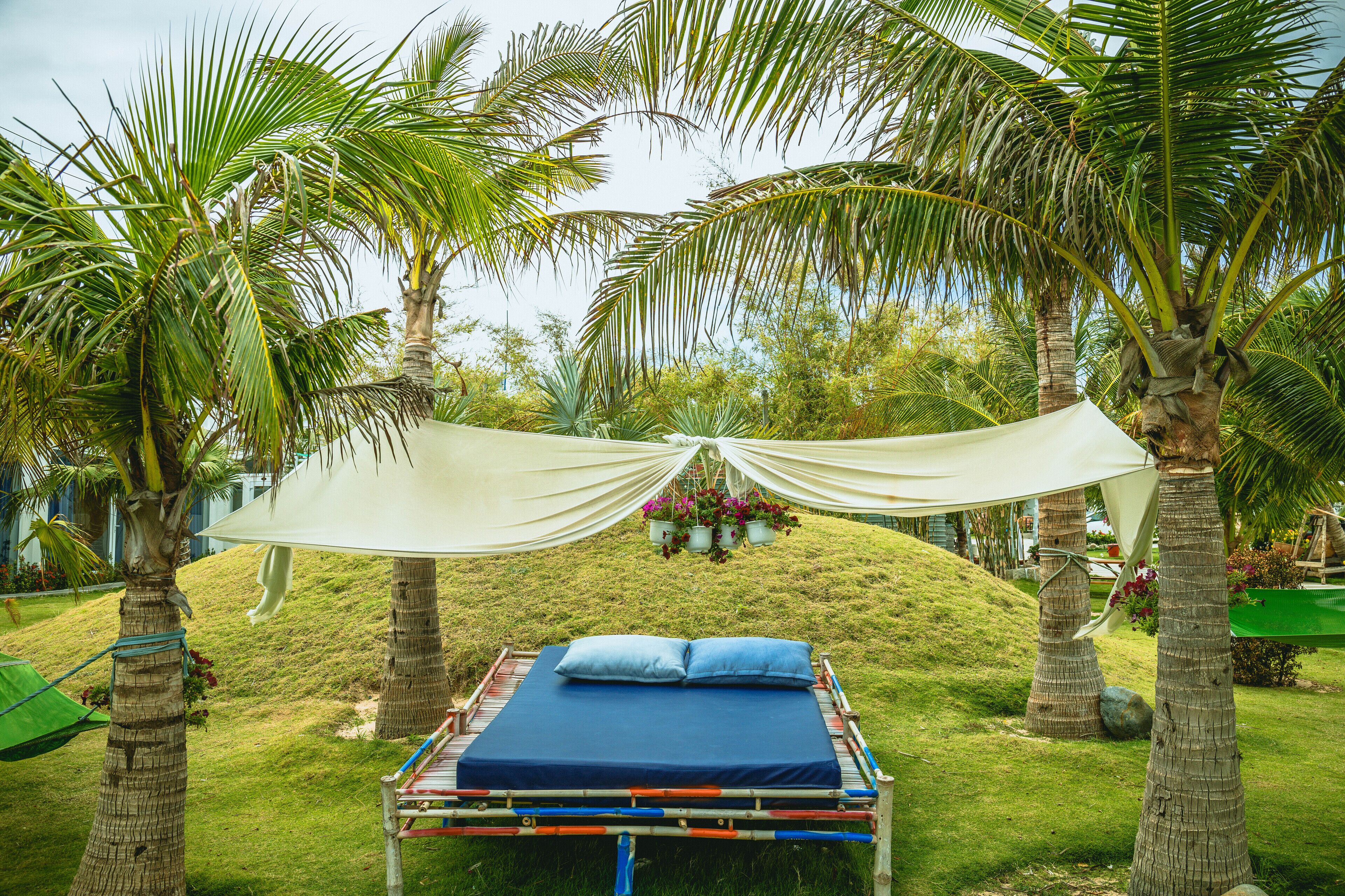 A bed with a blue mattress and pillows, surrounded by palm trees and a white canopy.