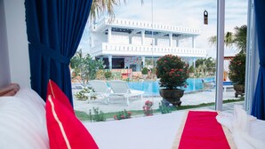 A hotel room with a view of a pool area, including lounge chairs and a building with a white facade. - Suoi TIen Hills Hotel (Mui Ne)
