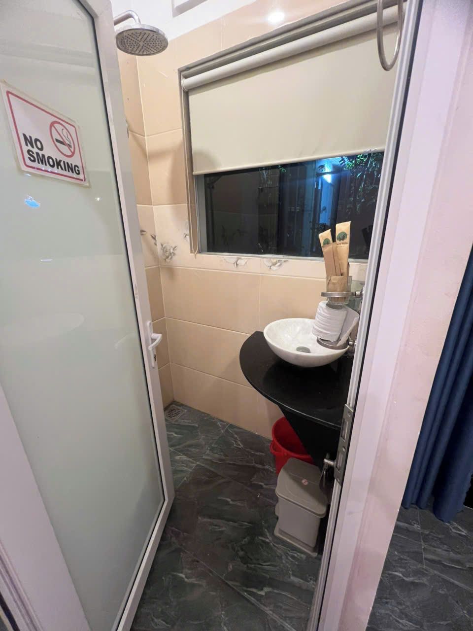 Une petite salle de bain avec une porte de douche en verre, un lavabo avec un bac blanc et un panneau « interdiction de fumer » sur le mur.