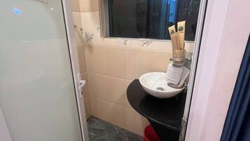 Une petite salle de bain avec une porte de douche en verre, un lavabo avec un bac blanc et un panneau « interdiction de fumer » sur le mur.