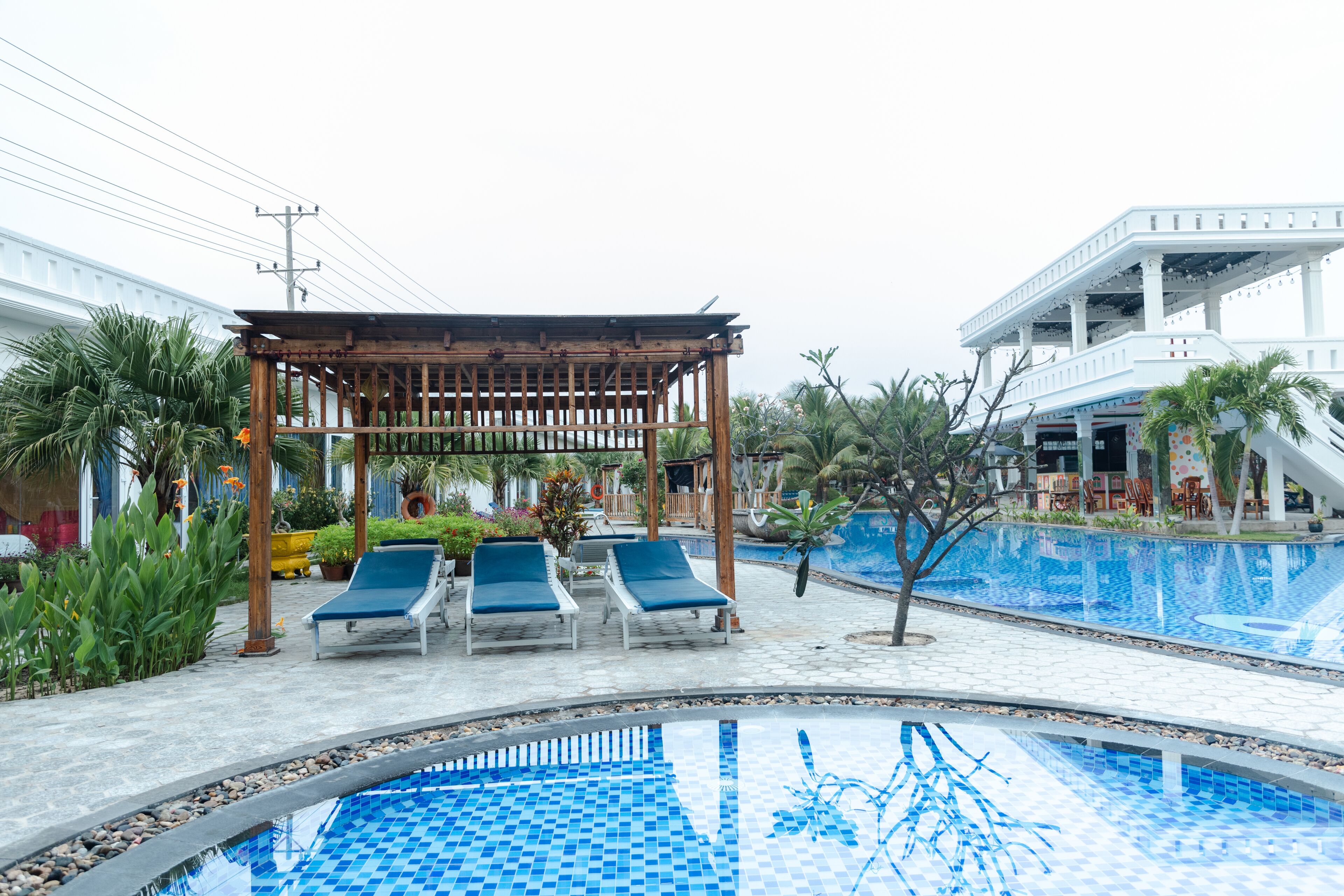 A pool area with lounge chairs, a wooden pergola, and a small waterfall feature.
