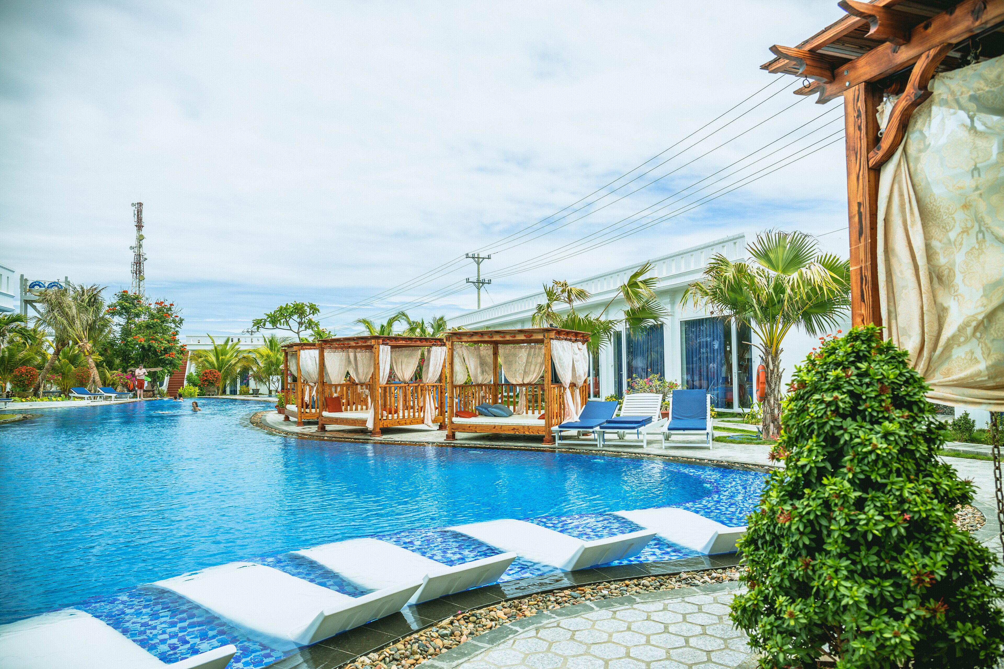 A swimming pool with lounge chairs, a wooden gazebo, and palm trees.