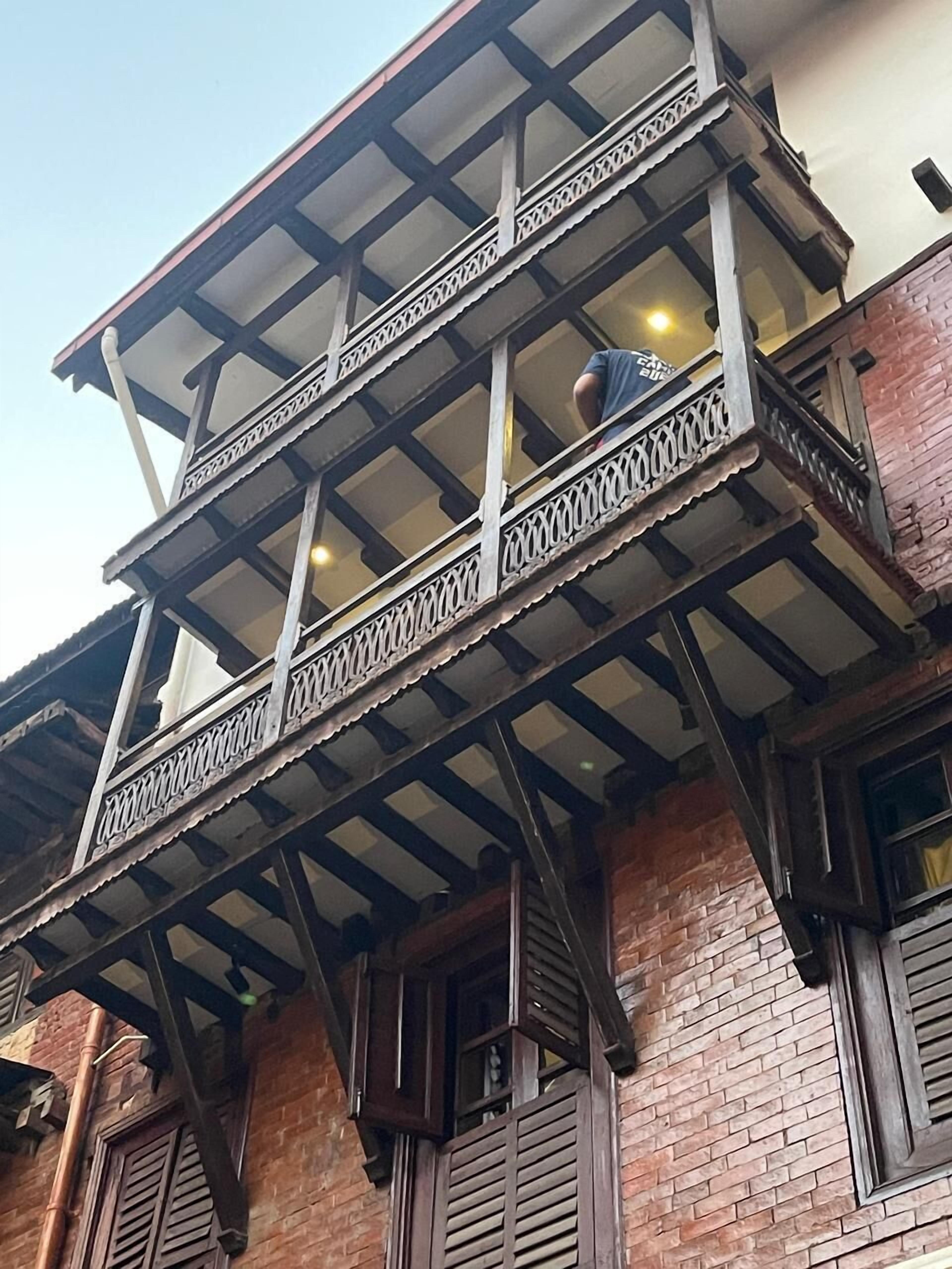 Un immeuble à plusieurs étages doté d’un balcon orné de rampes en métal finement travaillées et d’un plancher en bois.