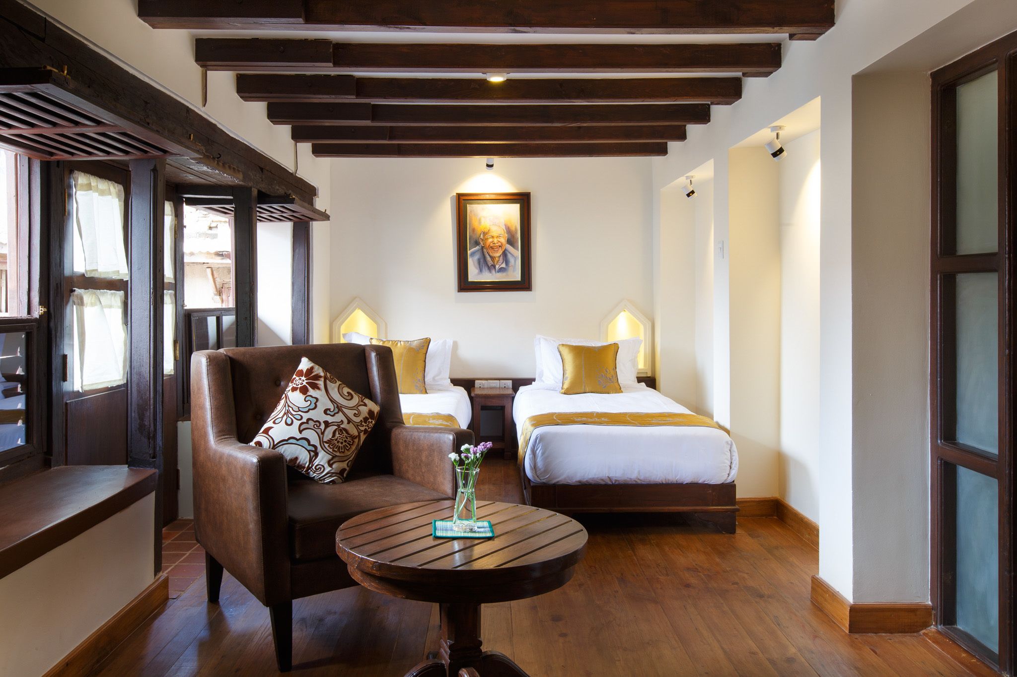 Une chambre d’hôtel avec un plafond en bois, un canapé agrémenté d’un coussin à motifs, une table ronde avec un vase et deux lits avec des lampes.