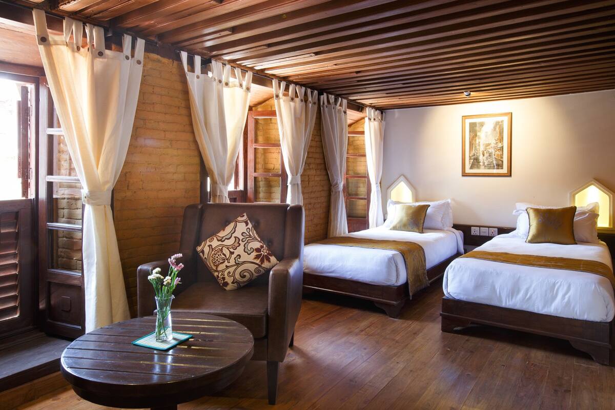 A room with two beds, a wooden ceiling, and a table with a vase of flowers.