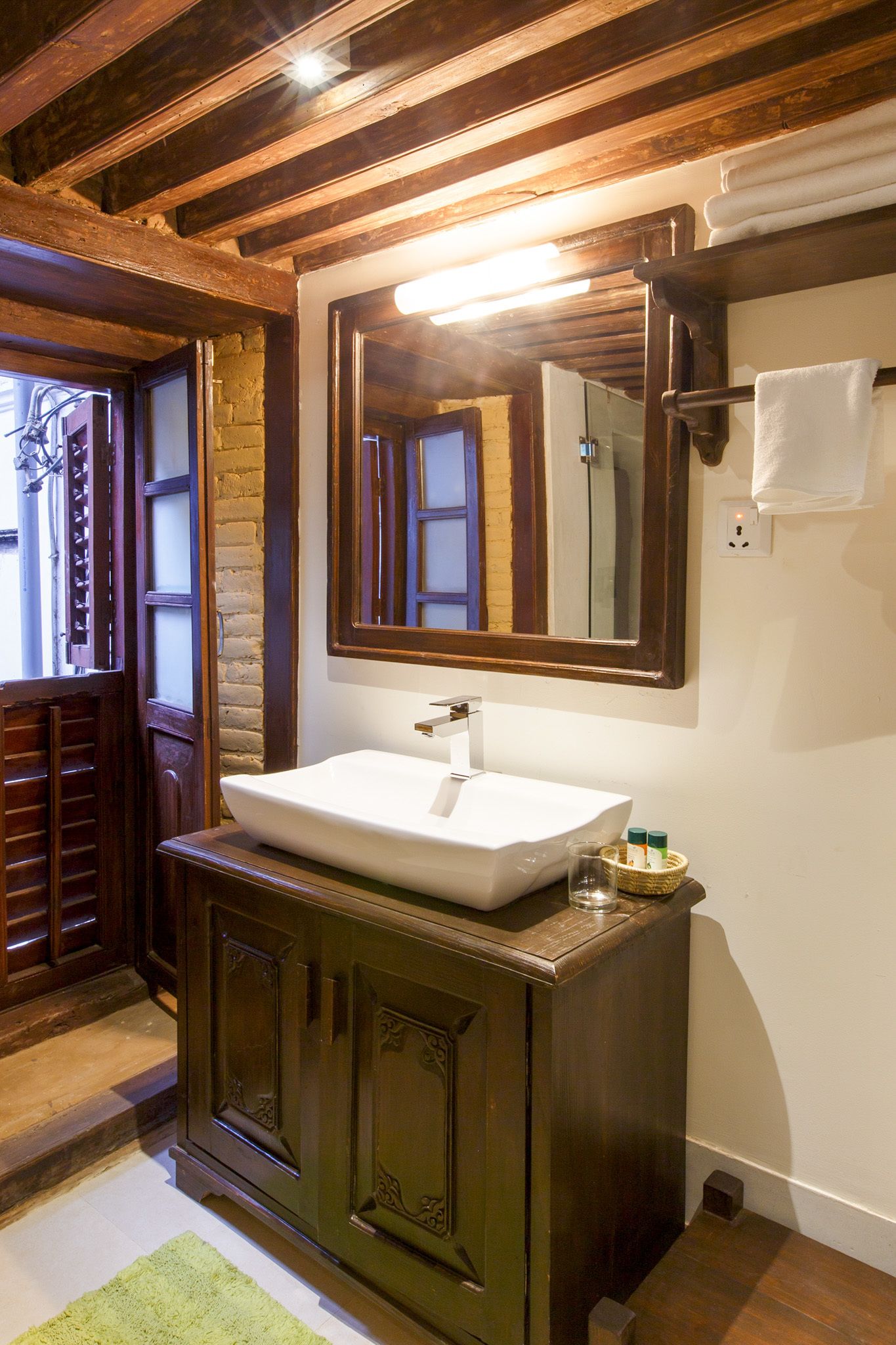 A bathroom with a wooden vanity, a white sink, a mirror, and a towel rack.