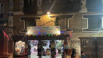 A traditional Nepalese shop with a signboard, various goods displayed outside, and a person sitting on a bench nearby.