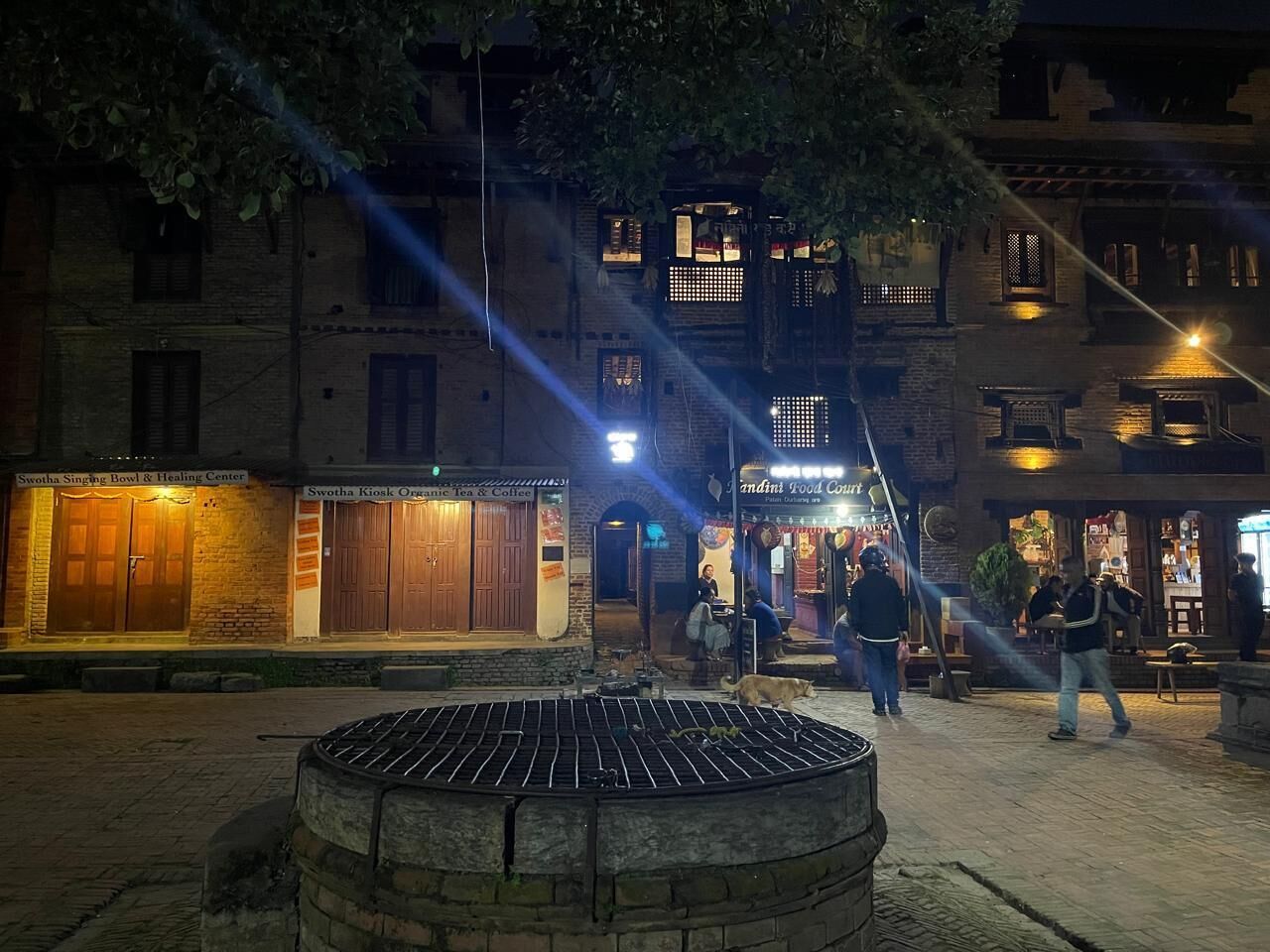 A courtyard with a central fire pit, surrounded by buildings with various shops and restaurants.