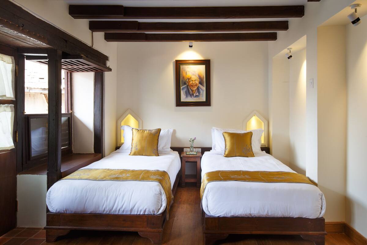 A hotel room with two beds, wooden headboards, white bedding, and a framed portrait on the wall.