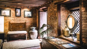 Una habitación rústica con paredes de ladrillo visto, un banco de madera, un jarrón grande y cuadros enmarcados en la pared.